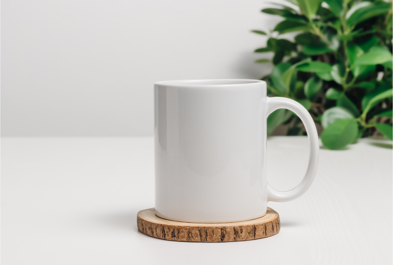 White mug on coaster, plant background.