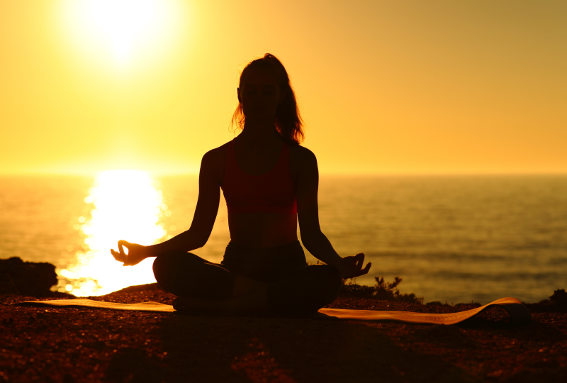 Silhouette meditating at sunset by the sea.
