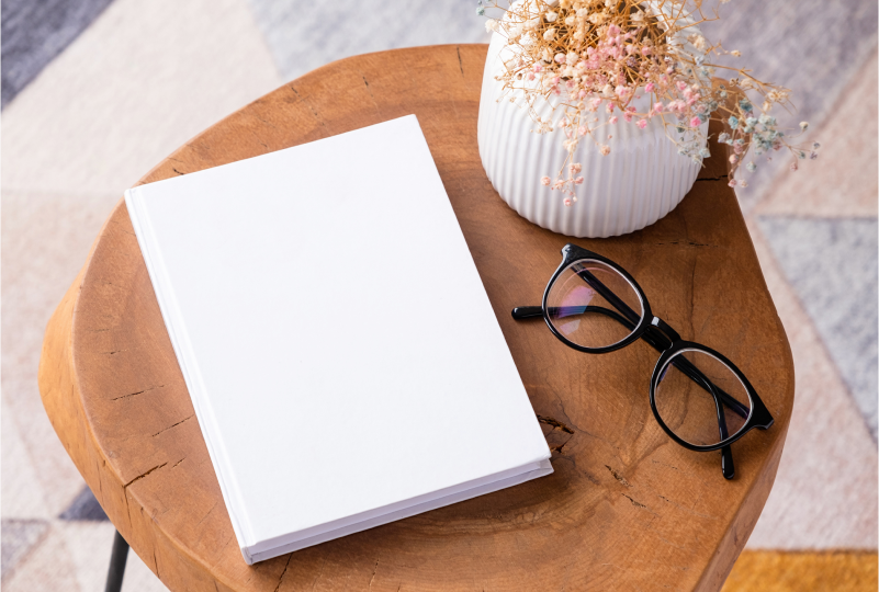 Book, glasses, and vase on wooden table.