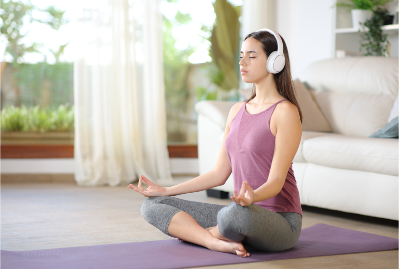 Woman meditating with headphones on yoga mat.